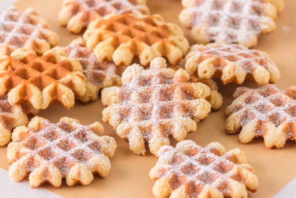 A cluster of golden-brown waffle cookies dusted with powdered sugar on parchment paper.