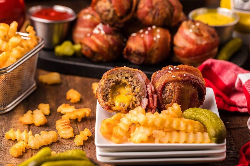 A plate with bacon wrapped cheeseburger bites and some fries.