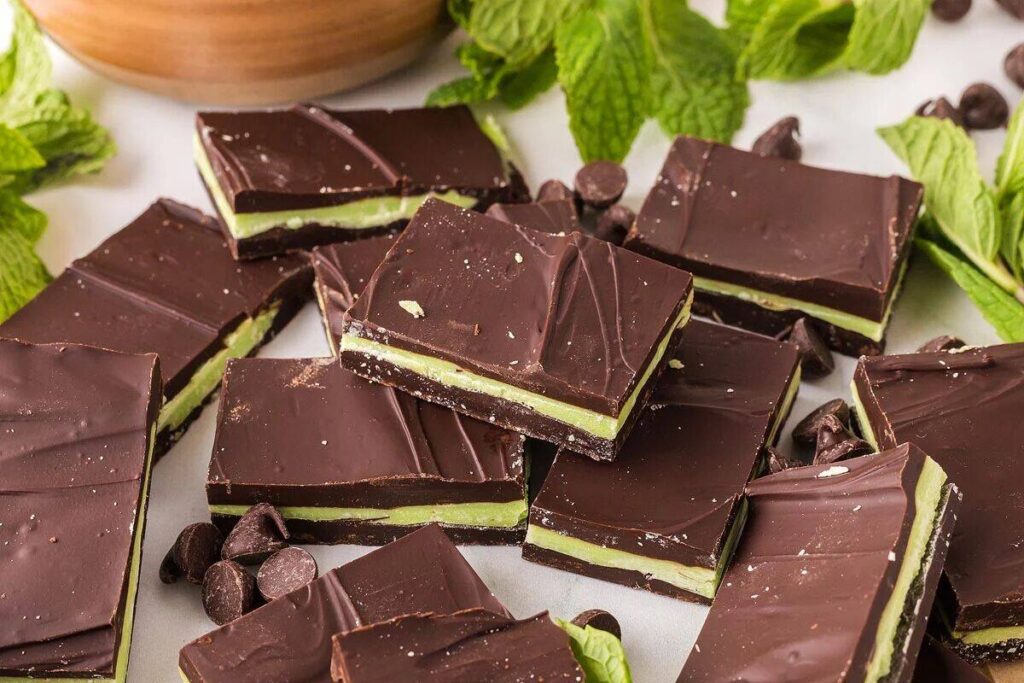 Homemade Andes mints elegantly arranged on a surface, surrounded by fresh mint leaves and chocolate chips.