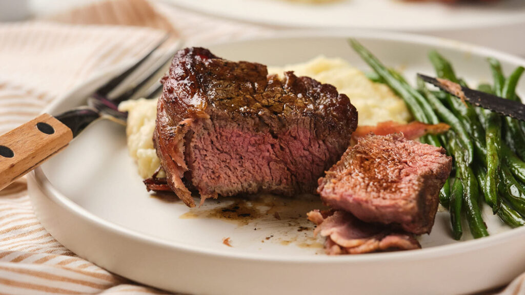 A plate of cooked beef steak, served with mashed potatoes and green beans.