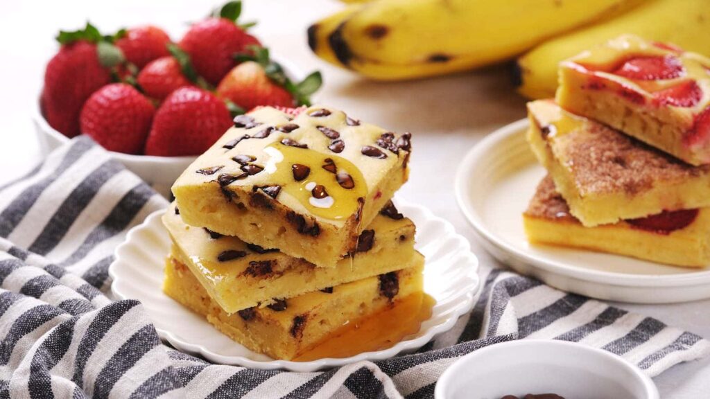 Baked pancakes topped with chocolate and fruit, stacked on a white dish.