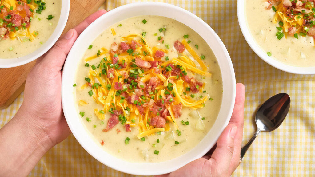 A bowl of creamy soup topped with bacon, shredded cheese, and chopped green onions.