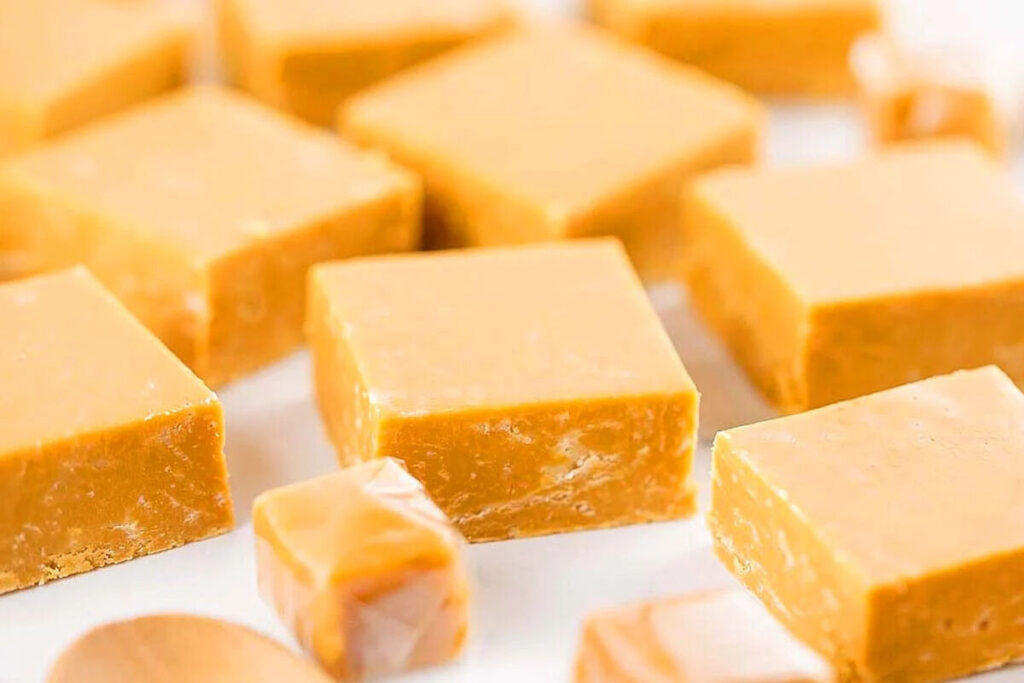 Caramel fudge squares rest on a white surface, highlighting a sweet, homemade dessert.