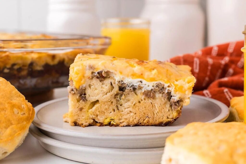 A slice of biscuits and gravy breakfast casserole with layers of bread, eggs, sausage, and cheese sits on a plate.
