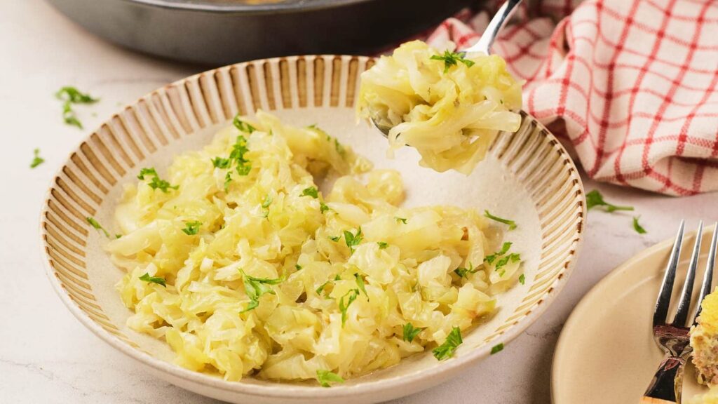 A bowl of cooked cabbage garnished with green herbs, with a fork resting beside it.