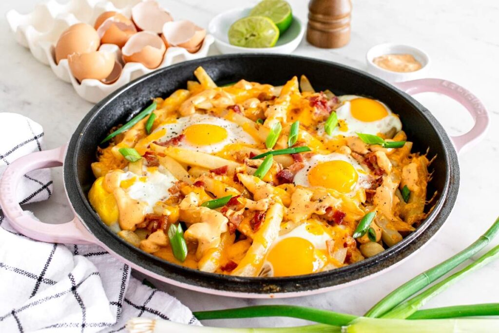 A breakfast skillet with sunny-side-up eggs sits on melted cheese, green onions, and crispy fries.