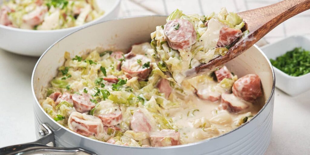 A wooden spoon lifting a portion of cabbage and sausage alfredo.