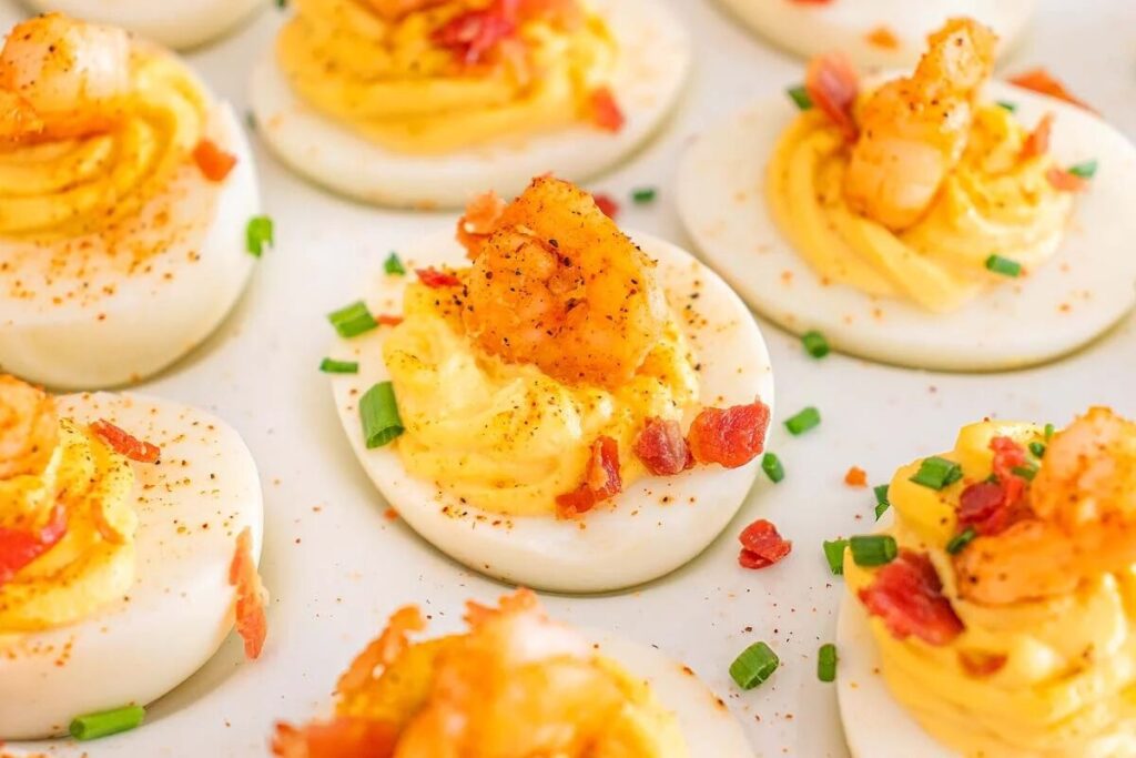 Cajun shrimp deviled eggs topped with bacon, chives, and a sprinkle of paprika.