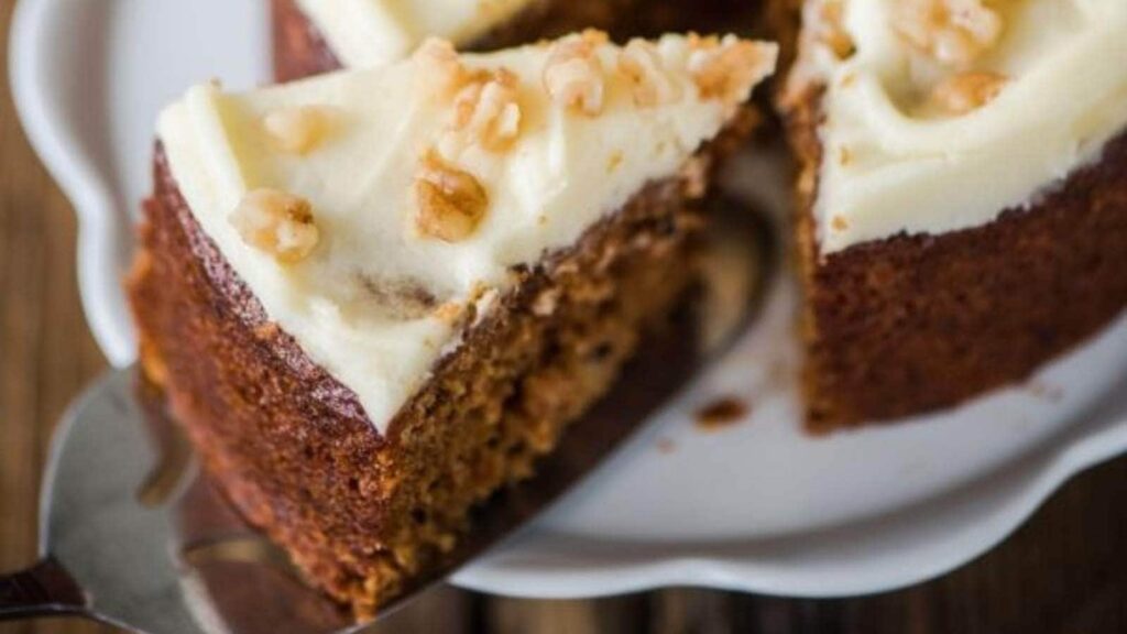 A spatula lifting a slice of carrot cake with white frosting.