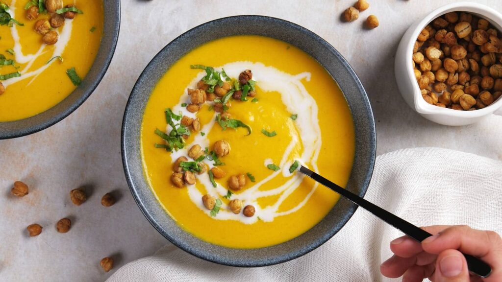 A top-down view of a bowl of carrot ginger soup garnished with herbs and cream.