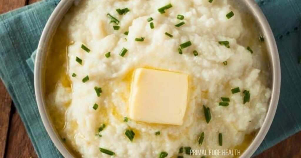A bowl of creamy mashed cauliflower topped with a pat of butter and garnished with chopped chives.