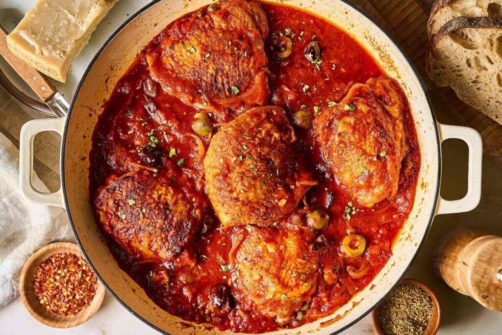 Chicken Puttanesca thighs simmered in tomato sauce with olives and herbs, served with bread.