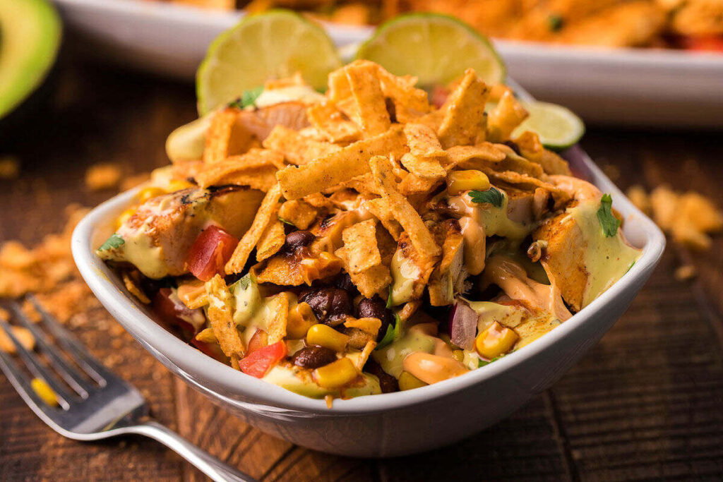 A Tex-Mex bowl with southwest salad, corn, black beans, avocado, tortilla strips, and creamy dressing, topped with lime.