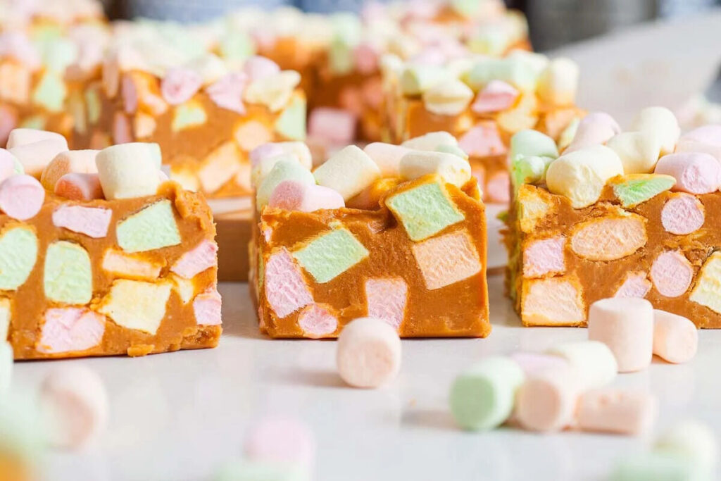 Three pieces of rocky road fudge with colorful mini marshmallows on a white surface.