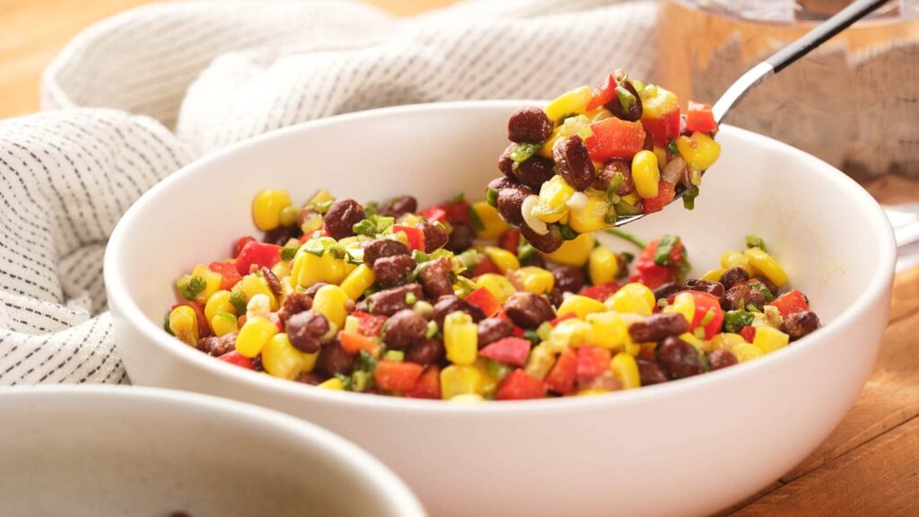 A bowl of black bean and corn salad garnished with diced red peppers and herbs.