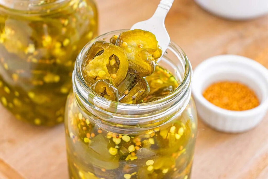 A close-up of jarred sliced jalapeños held by a fork above an open jar