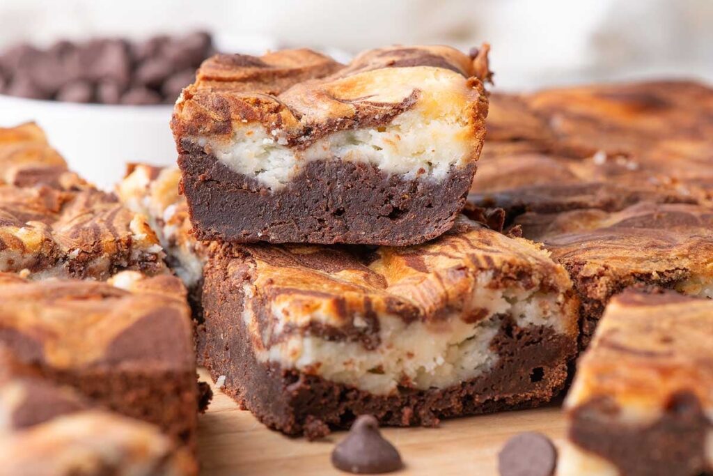 A stack of cream cheese brownies on a wood surface.