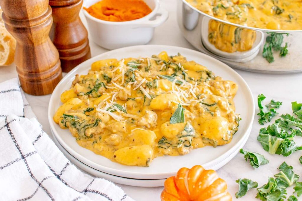 A plate of creamy pumpkin sausage gnocchi topped with shredded cheese and garnished with herbs.