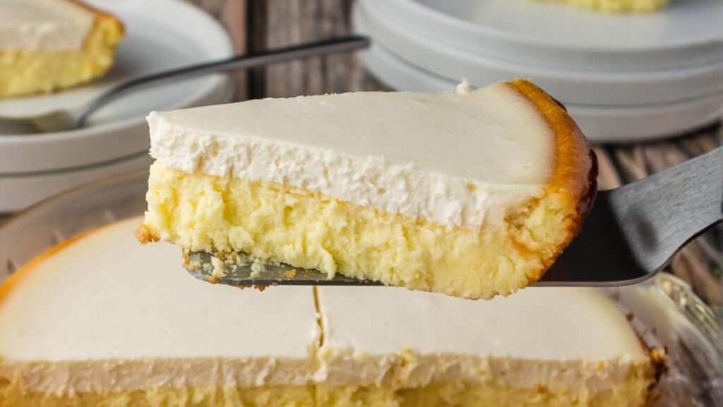 A slice of cheesecake being lifted with a spatula, showing creamy filling and a golden crust.