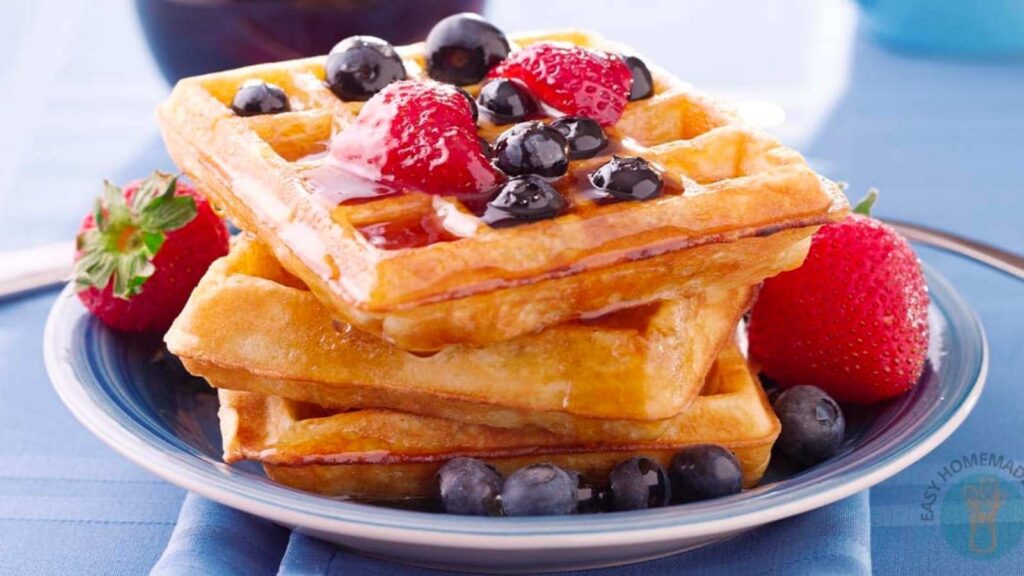 A plate of stacked waffles topped with strawberries, blueberries, and a drizzle of syrup.