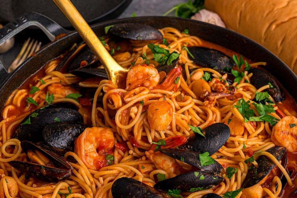 Spaghetti Frutti di Mare with mussels and shrimp in tomato sauce, topped with parsley in a pan with a gold fork.