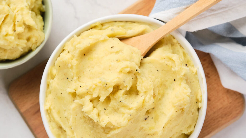 A bowl of creamy mashed potato resting on a wooden board.