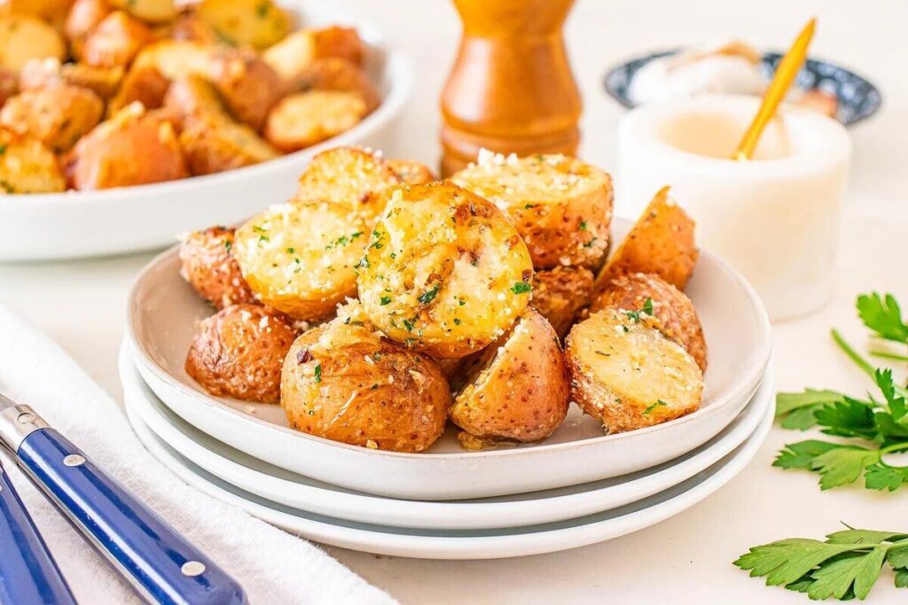 A plate of garlic parmesan roasted potatoes garnished with herbs and cheese.