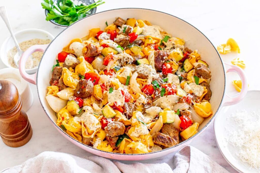 Garlic parmesan steak tortellini with cherry tomatoes and zucchini, topped with melted cheese and parsley.