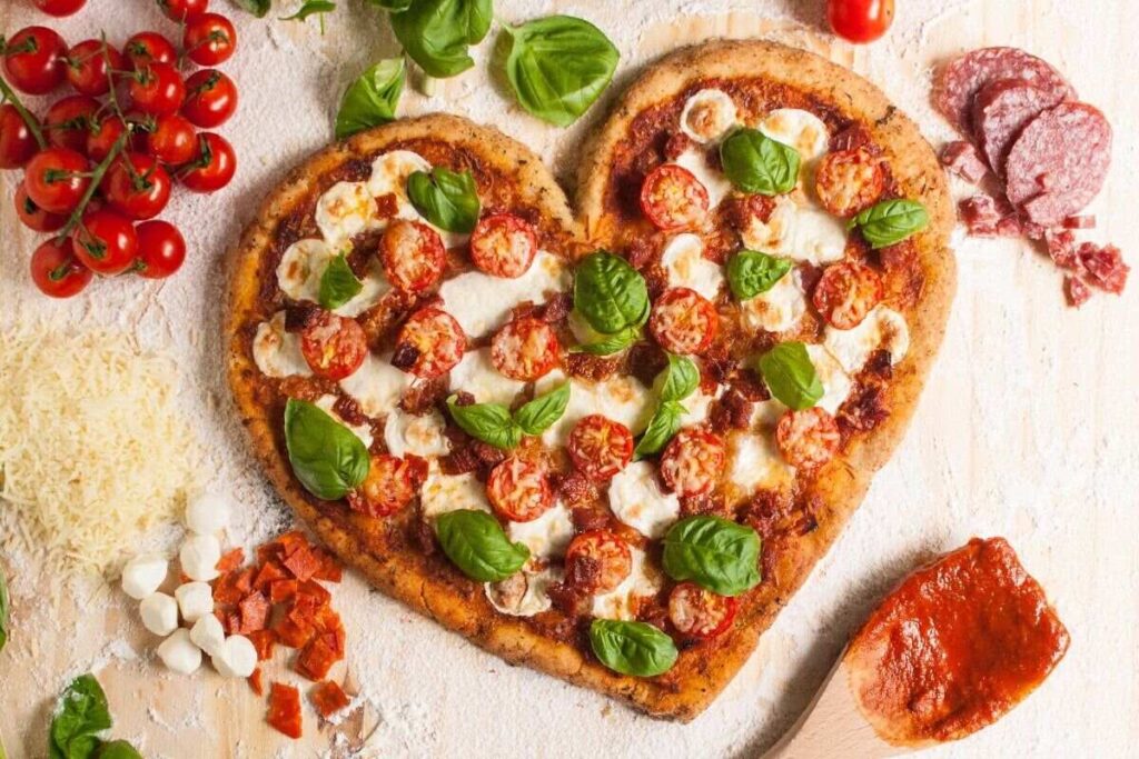 Heart-shaped pizza with tomatoes, mozzarella, basil, and salami.