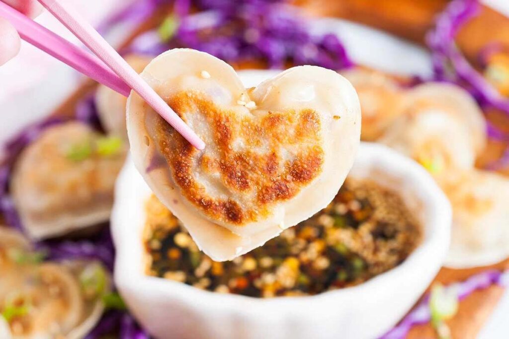 A Valentine's potstickers held with chopsticks over a blurred table.