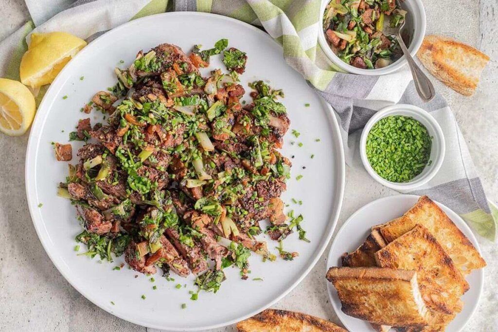 Grilled New York steak on a white plate with herbs and vegetables, served with toasted bread and small bowls of garnishes.