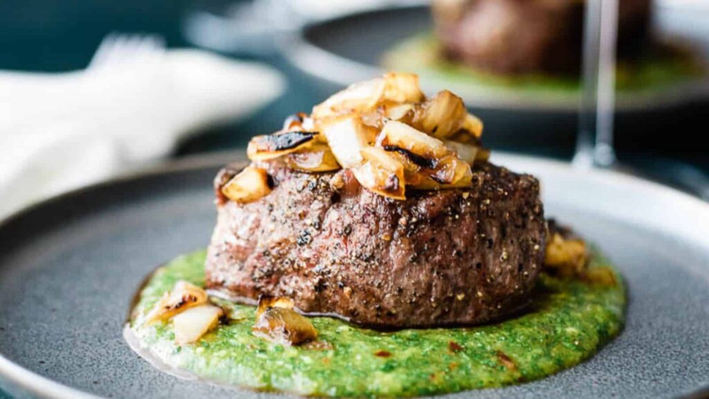 Closeup of a filet mignon with green sauce on a gray plate.
