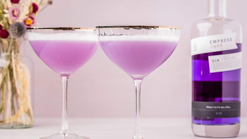 Two empress 1908 gin sours next to a bottle of purple gin.