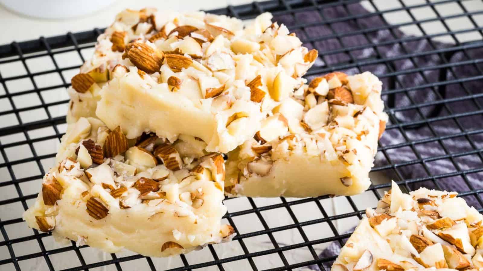 Four pieces of almond-topped white fudge rest on a cooling rack.