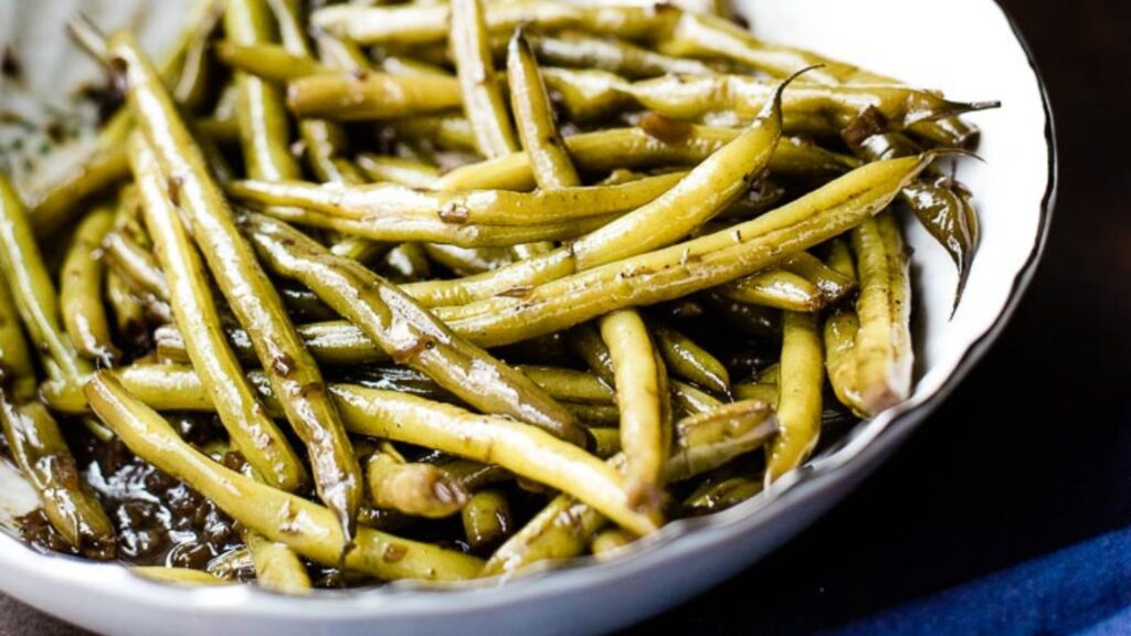 Overhead shot of worcestershire green beans in a white serving bowl next to a blue towel.