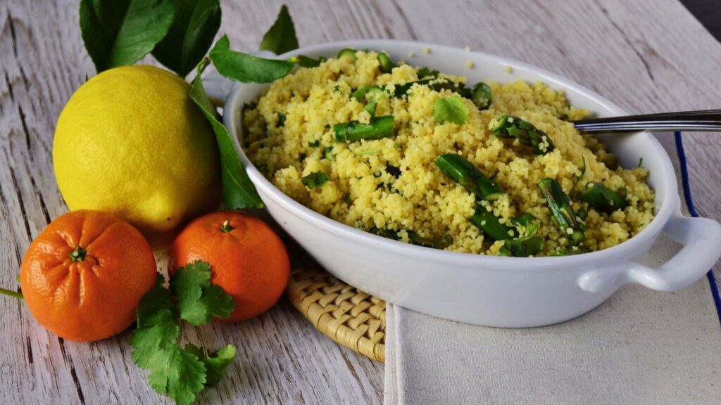 Citrus asparagus couscous in a white bowl next to an orange and lemons.