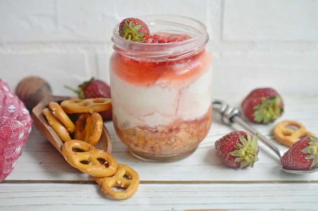 Jar of dessert with strawberries and pretzels.