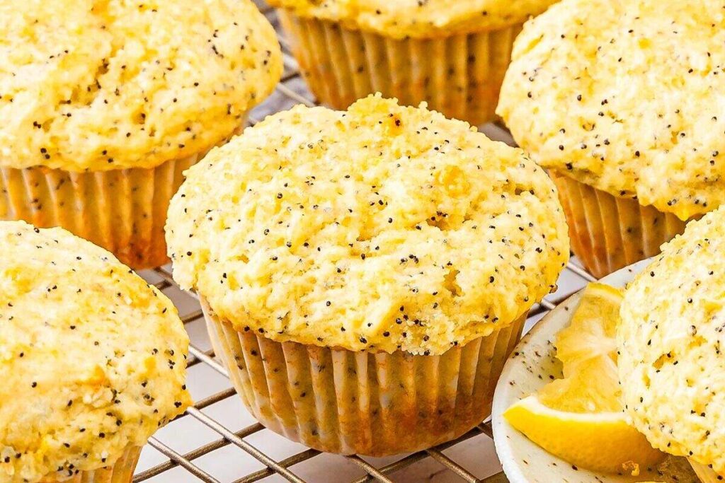 Close-up of lemon poppy seed muffins on a cooling rack, with fresh lemon wedges adjacent.