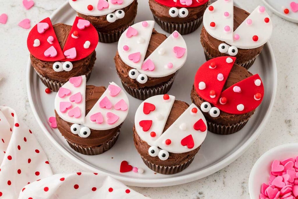 Love bug cupcakes with red and pink fondant wings, candy eyes, and heart decorations.