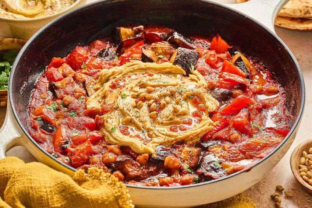 Mediterranean chickpea skillet with roasted eggplant, red peppers, hummus, herbs, and pine nuts.