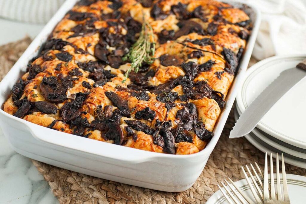 Baked mushroom focaccia topped with fresh herbs, served with plates and utensils.