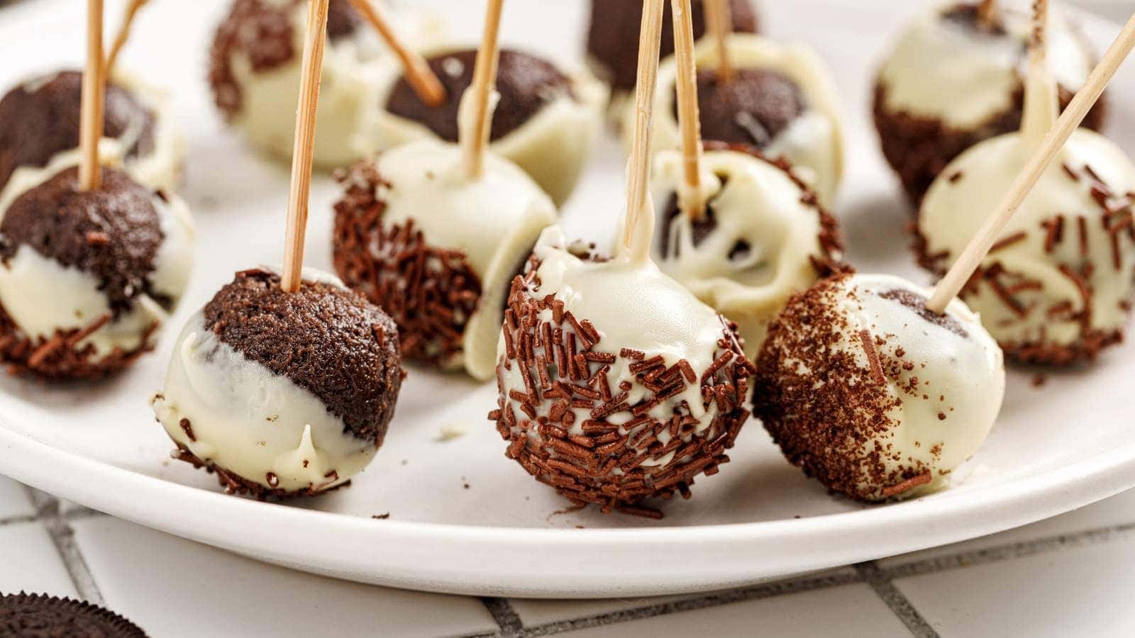 A white plate with Oreo cake pops covered in white chocolate and chocolate sprinkles.