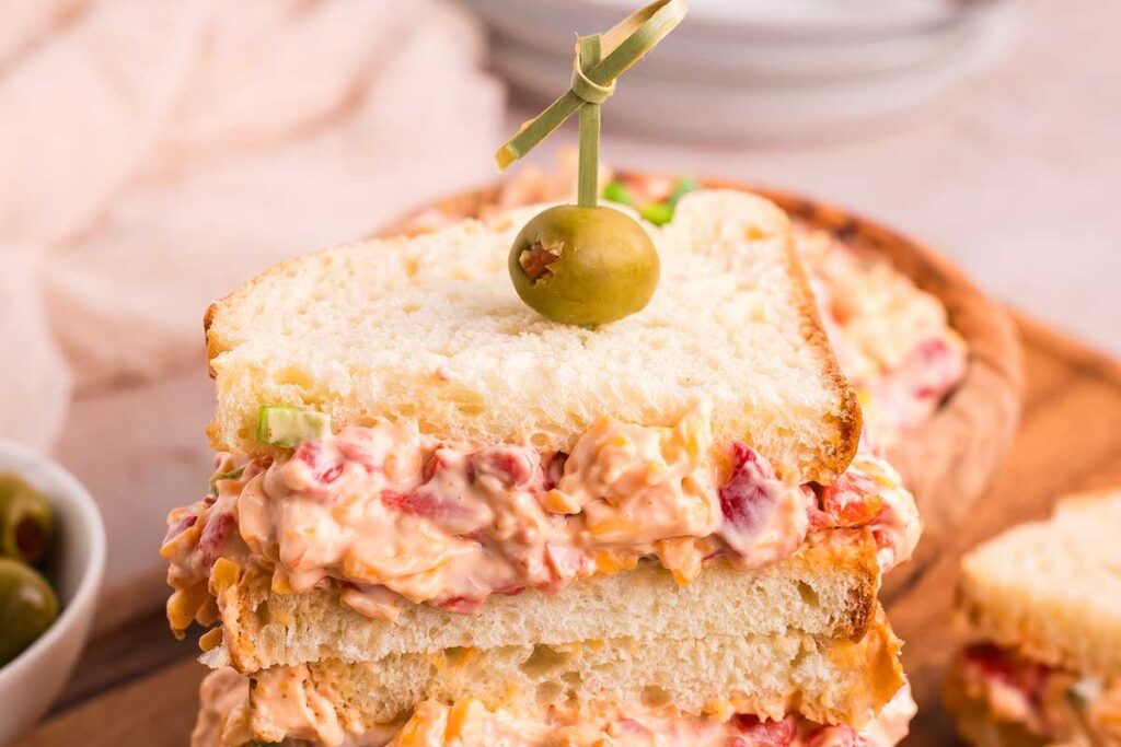 A sandwich with a green olive and pimento cheese on top.