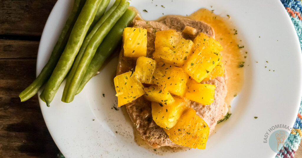 A plate with a serving of meat topped with pineapple chunks and garnished with spices.
