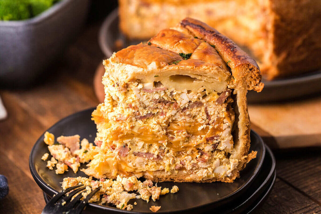 A close-up of a savory layered pie with a flaky crust, filled with meat, cheese, and vegetables.