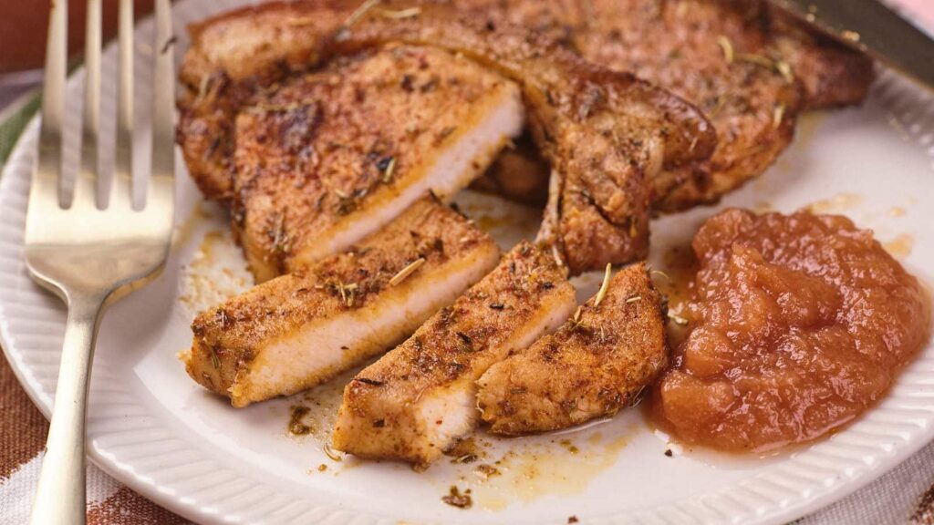 Pork chops and applesauce on a white plate.