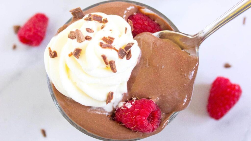 A glass of protein chocolate pudding garnisehd with raspberries and whipped cream.