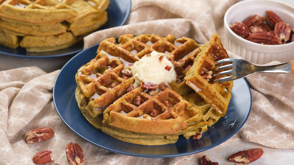 A plate of pumpkin waffles topped with a dollop of cream and pecans.