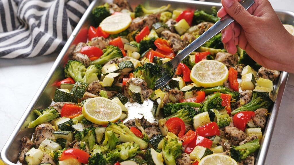 Cooked chicken, various vegetables and lemon slices on a sheet pan.