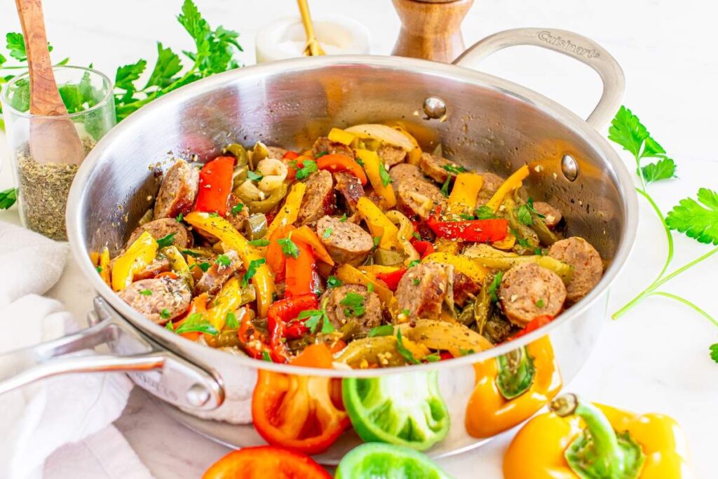 A skillet filled with cooked Italian sausage slices, red, green and yellow bell peppers, and green herbs.